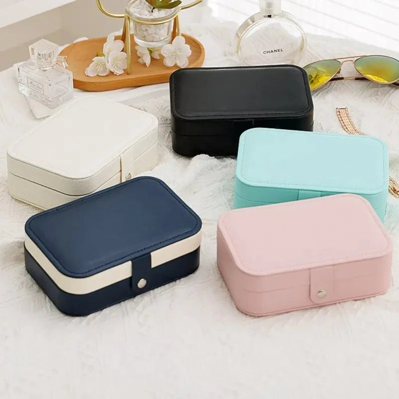 Set of colorful jewelry boxes on a soft surface with a Chanel perfume bottle in the background.