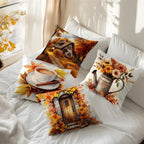 Four decorative throw pillows with autumn-themed prints arranged on a bed with white bedding. The prints include a cabin scene, a cup of coffee with leaves, a watering can with flowers, and a wooden door surrounded by leaves.