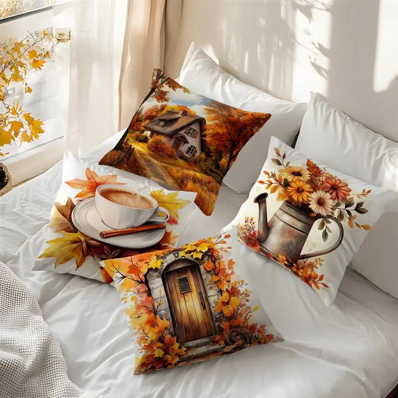 Four decorative throw pillows with autumn-themed prints arranged on a bed with white bedding. The prints include a cabin scene, a cup of coffee with leaves, a watering can with flowers, and a wooden door surrounded by leaves.