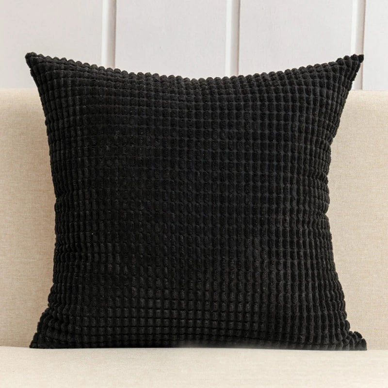 Black textured pillow on a beige couch with a white wall background