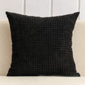 Black textured pillow on a beige couch with a white wall background