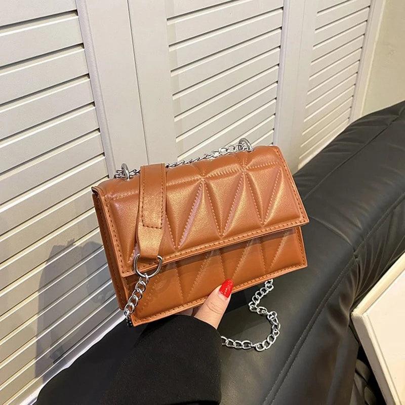 Brown quilted handbag with a chain strap held by a person against a neutral background