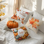 Four decorative throw pillows with autumn and pumpkin designs arranged on a white bed in a softly lit bedroom. The pillows feature illustrations of pumpkins, fall leaves, and the words 'Hello Pumpkin' and 'Thankful'.