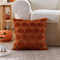 An orange-brown throw pillow with a 3D textured pumpkin pattern and green stems, styled on a patterned rug in a cozy living room setting next to a white armchair and a jack-o'-lantern.