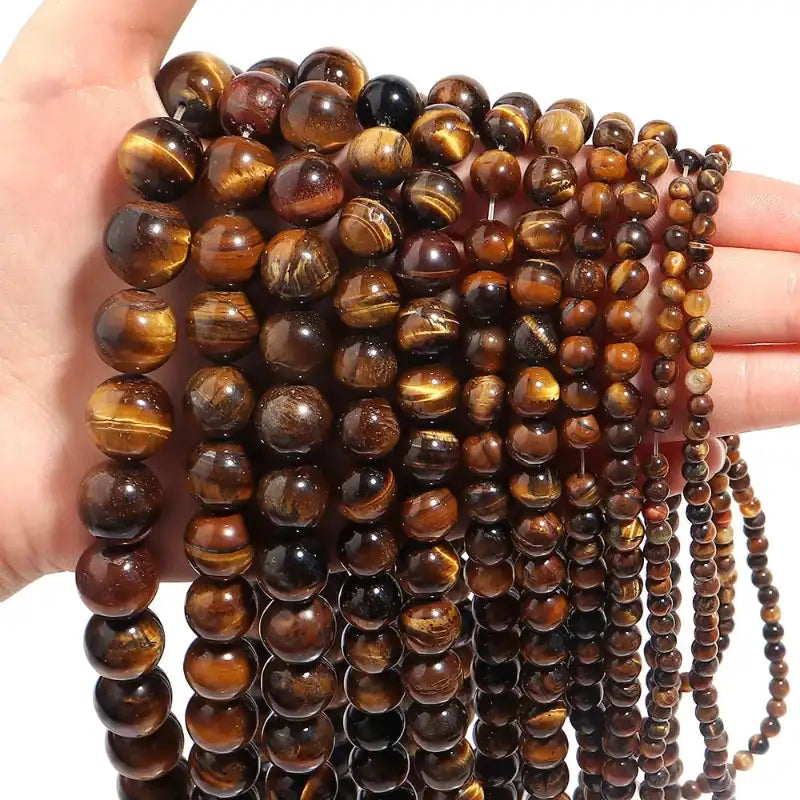 Close-up of a hand holding a string of tiger eye beads against a white background