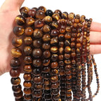 Close-up of a hand holding a string of tiger eye beads against a white background