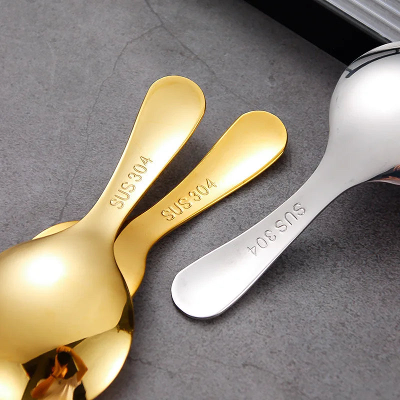 Two gold and one silver spoon on a gray surface with 'SUS 304' text.
