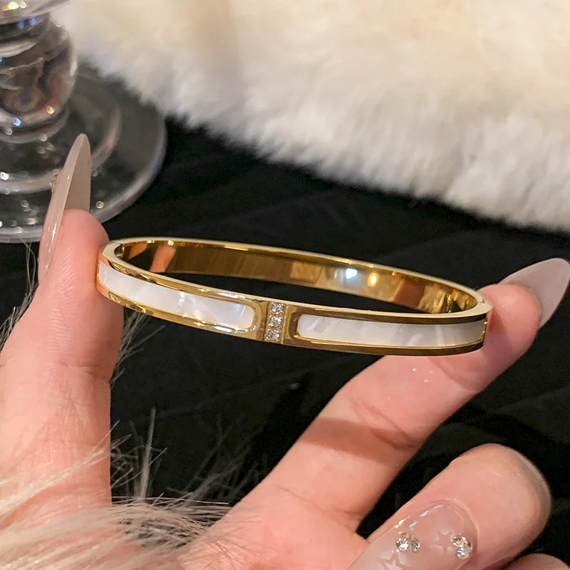 Gold bracelet with white stones held by a hand against a blurred background