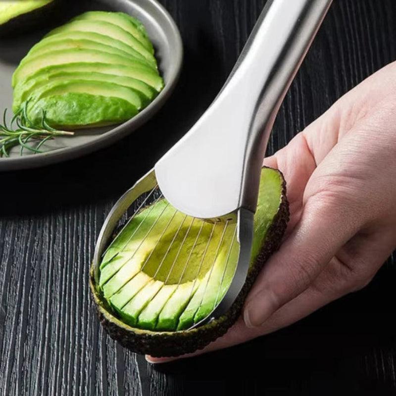 Avocado slicer being used to slice an avocado on a dark surface with sliced avocados in the background.