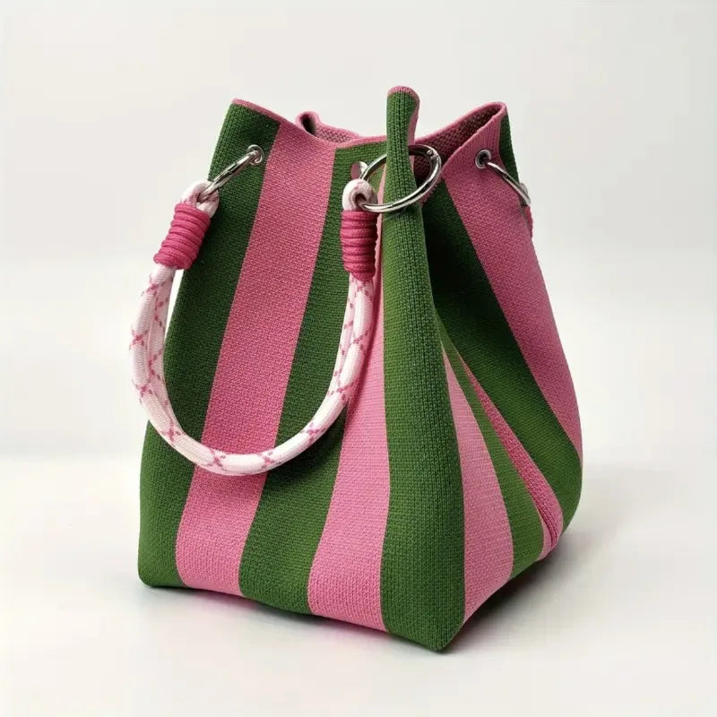 A canvas bucket bag with vertical pink and green stripes, featuring a thick pink-and-white patterned rope handle and silver metal hardware, photographed on a clean white background.