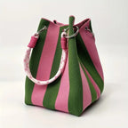 A canvas bucket bag with vertical pink and green stripes, featuring a thick pink-and-white patterned rope handle and silver metal hardware, photographed on a clean white background.