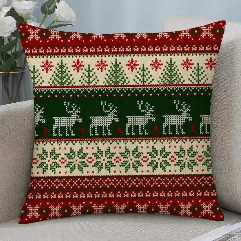 A square throw pillow with a festive Christmas knit pattern in red, green, and cream, resting on a light gray sofa.