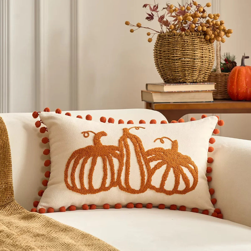 Decorative pillow with pumpkin design on a couch, with a vase of flowers and books in the background.