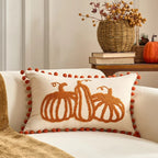 Decorative pillow with pumpkin design on a couch, with a vase of flowers and books in the background.