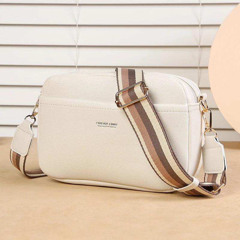 Beige handbag with a striped strap on a beige surface