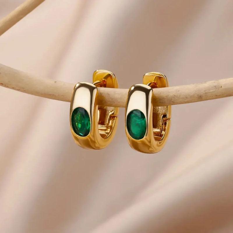 Gold hoop earrings with green gemstones on a beige background