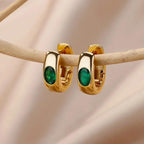 Gold hoop earrings with green gemstones on a beige background