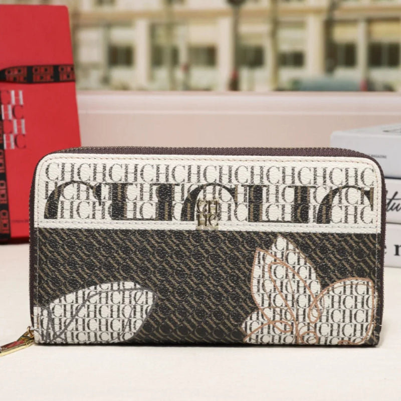 A Dior wallet with a black and white monogram pattern, featuring a signature heart motif on the front, displayed on a tabletop with a blurred background.