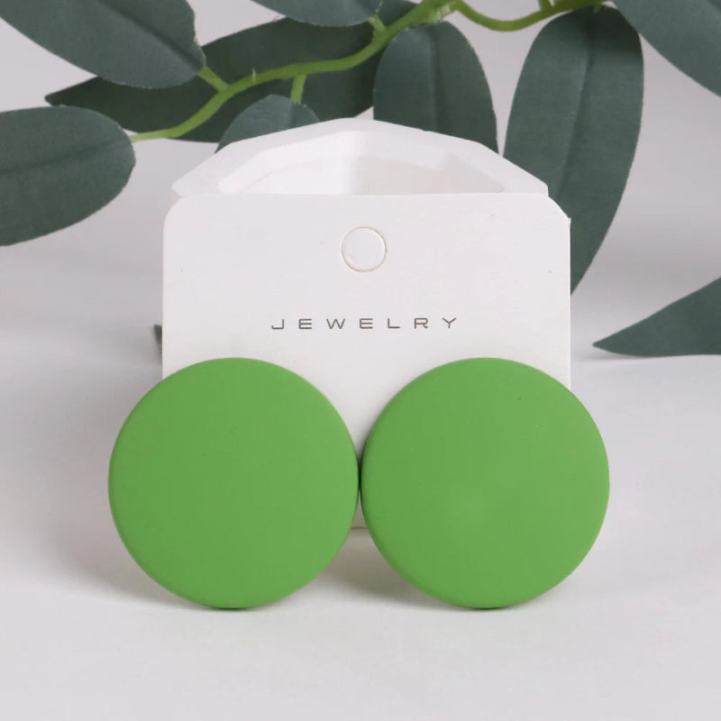 Green round earrings on a jewelry card with green leaves in the background