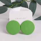 Green round earrings on a jewelry card with green leaves in the background
