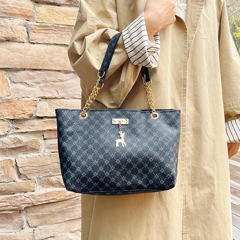 Person holding a blue patterned handbag with a gold chain strap against a stone wall.