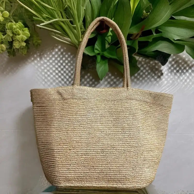 Woven straw bag on a textured surface with green plants in the background