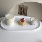 Tray with a glass of milk, a small cake, and a candle on a white surface.