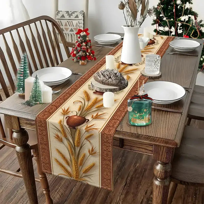 A rectangular woven table runner with a beige and brown holiday wheat design is styled on a wooden dining table. The table is set with white plates, candles, a white pitcher, and small decorative Christmas trees, with a Christmas tree visible in the background.