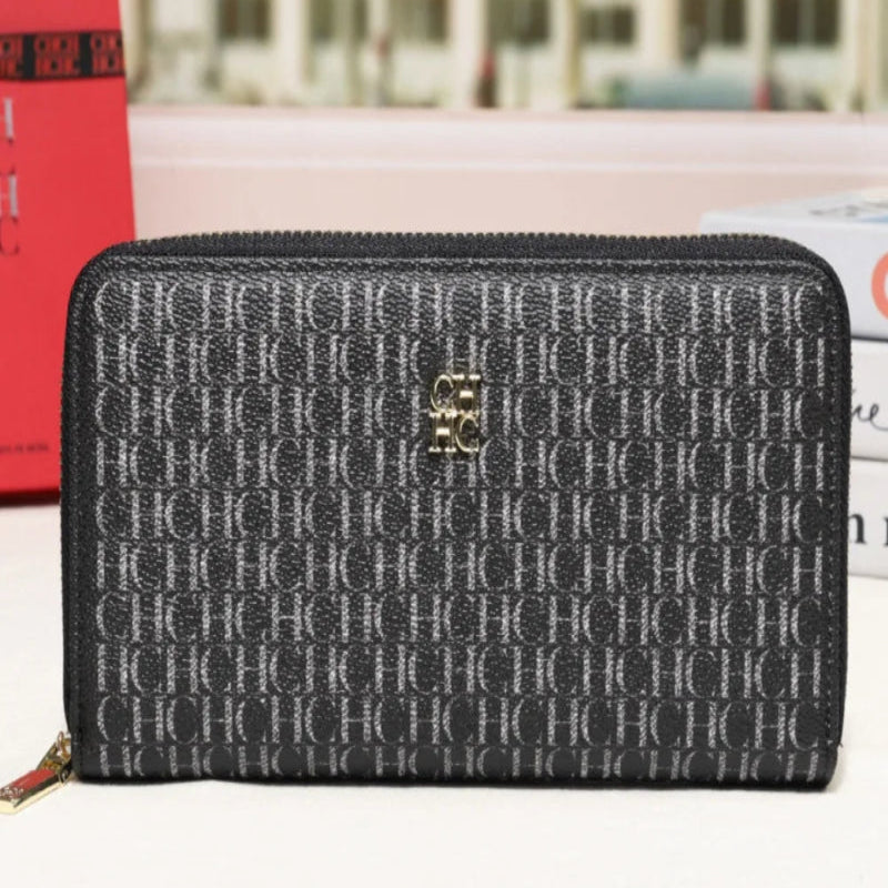 A black and gray monogram zip-around wallet with a gold-tone logo clasp, displayed on a white surface with a blurred city street background.