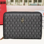 A black and gray monogram zip-around wallet with a gold-tone logo clasp, displayed on a white surface with a blurred city street background.