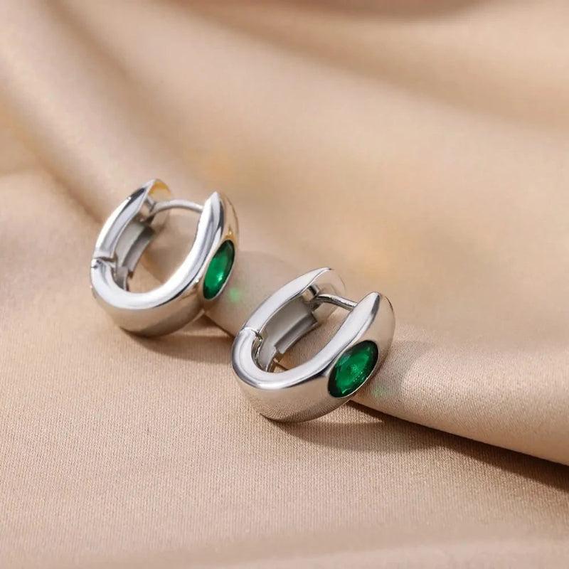 Silver hoop earrings with green gemstones on a beige fabric background