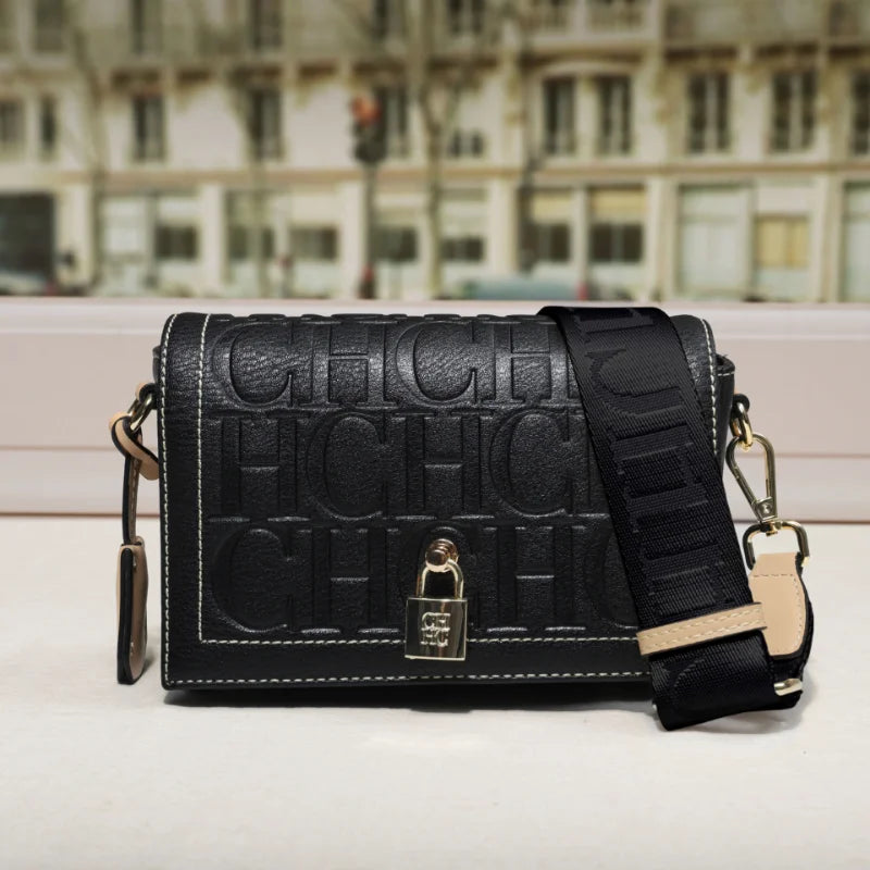 Black embossed handbag with a strap on a light surface with a blurred cityscape background