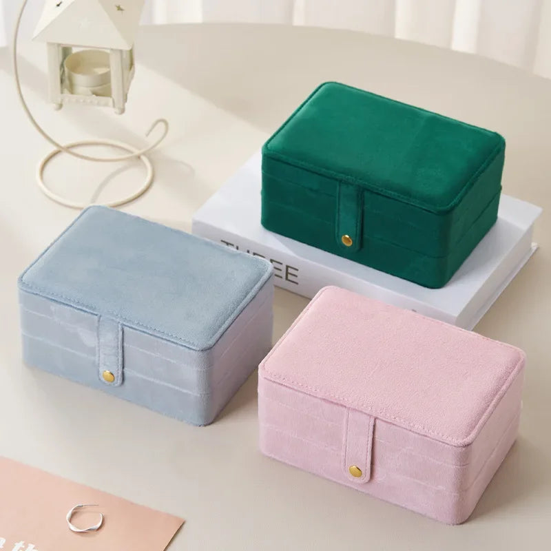 Three small fabric jewelry boxes in green, pink, and blue on a light surface.
