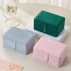 Three small fabric jewelry boxes in green, pink, and blue on a light surface.