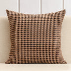 Brown textured pillow on a beige couch with a white paneled wall background