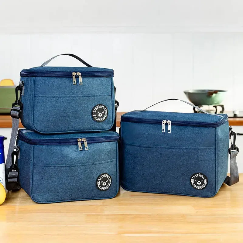 Set of three blue insulated lunch bags on a wooden surface with a blurred kitchen background.