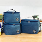 Set of three blue insulated lunch bags on a wooden surface with a blurred kitchen background.