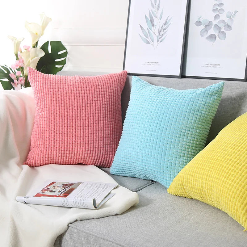 Three colorful textured pillows on a sofa with a magazine and decorative elements.