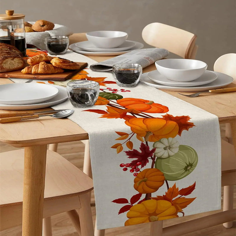 Dining table set with a floral and harvest-themed table runner, plates, bowls, and glasses.