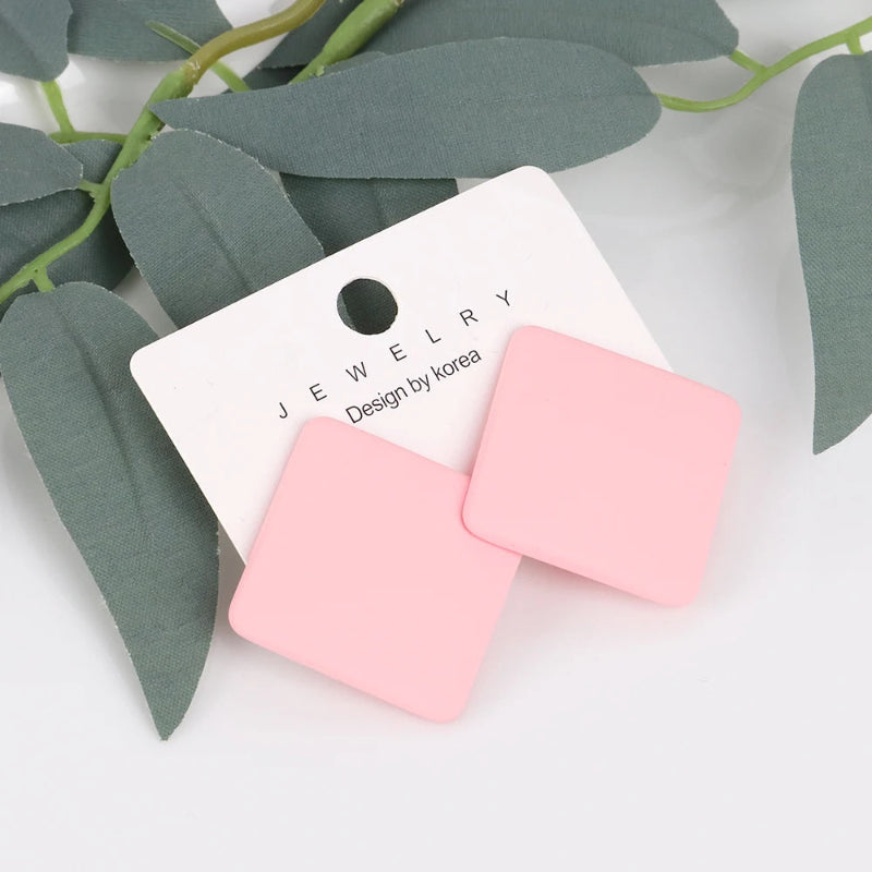 Pink square earrings on a jewelry card with green leaves in the background