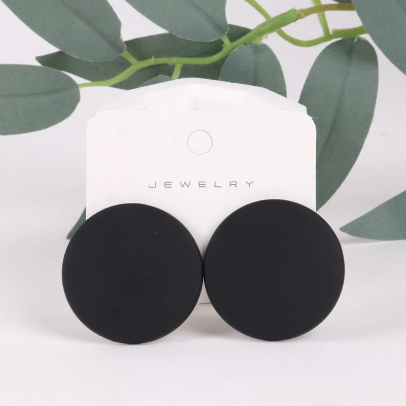 Black round earrings on a white jewelry card with green leaves in the background