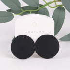 Black round earrings on a white jewelry card with green leaves in the background