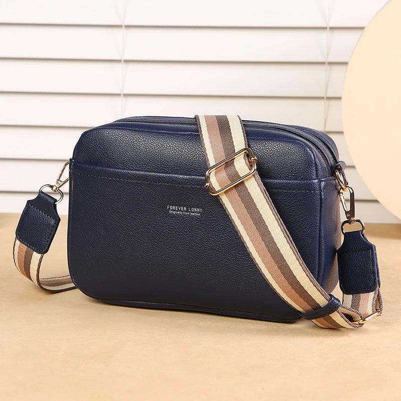 Navy blue handbag with a striped strap on a beige surface