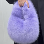 Person holding a fluffy purple handbag against a neutral background