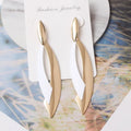 Gold earrings on a white card with 'Fashion Jewelry' text, placed on a decorative surface.