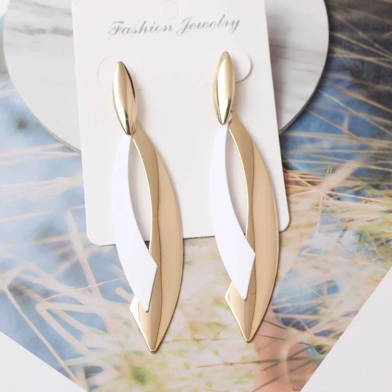 Gold earrings on a white card with 'Fashion Jewelry' text, placed on a decorative surface.