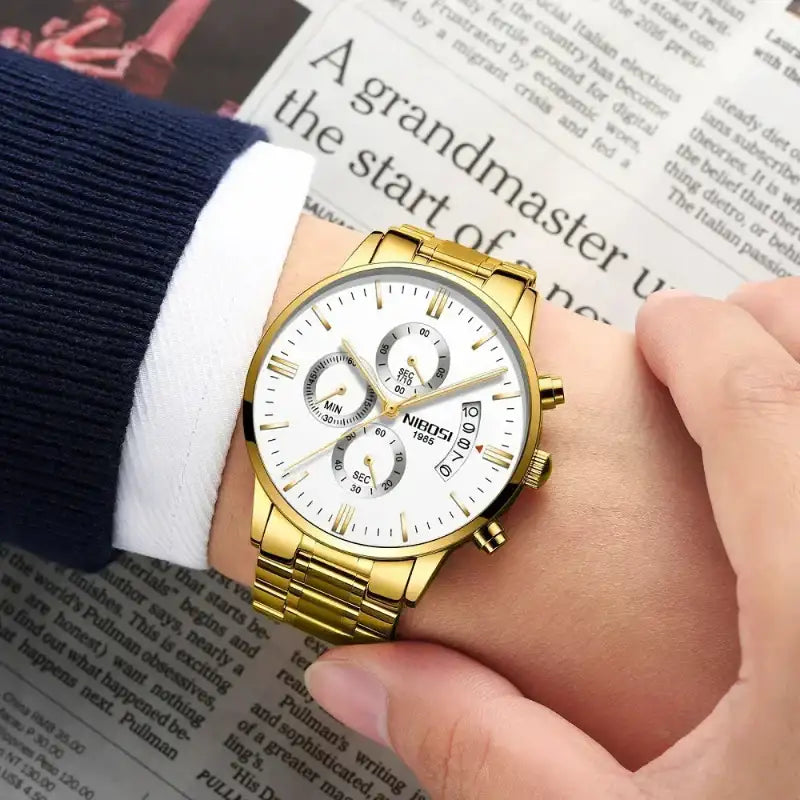Gold wristwatch on a person's wrist with a newspaper background