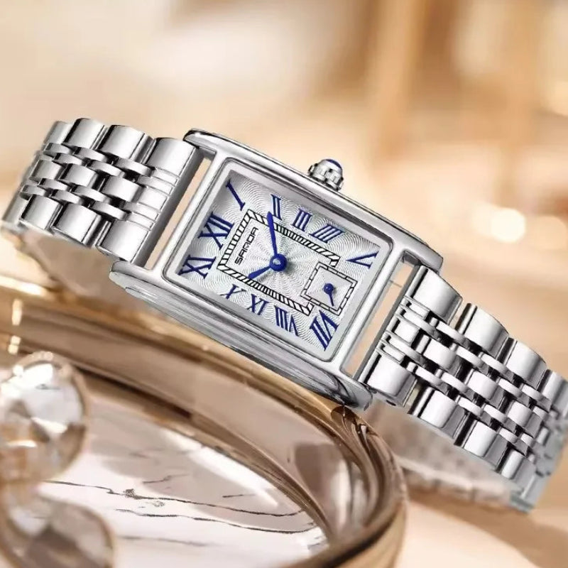 Silver watch with blue Roman numerals on a blurred background, featuring the brand 'SANDA'.