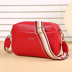 Red handbag with a striped strap on a beige surface