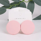 Pink earrings on a jewelry card with green leaves in the background